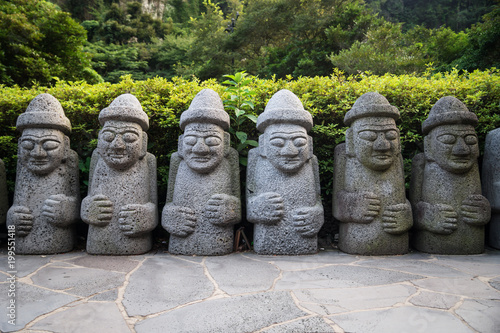 Dol Hareubang statues in a row in green forest, Seogwipo, Jeju Island, South Korea photo