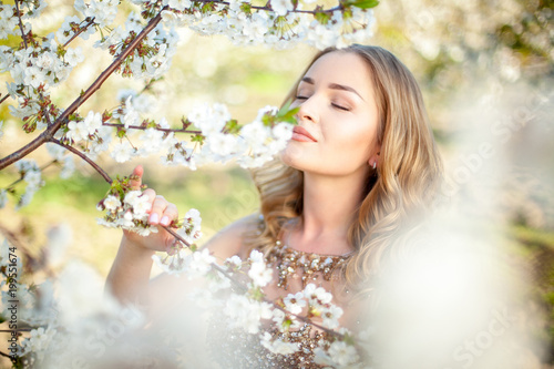 Spring. Close-up horyzontal portrait of a beautiful girl inhaling aroma of blooming tree in garden. Artwork. Copy space. Sotf focus