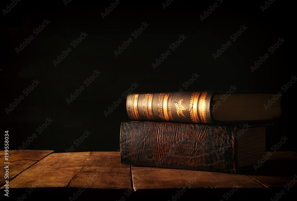 image of stack of antique books over wooden table and dark background.
