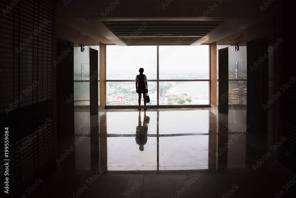 Fototapeta premium Silhouette view of young tourist Asian girl standing close to large glass window plan for adventure with beautiful tropical summer aerial view of city background.