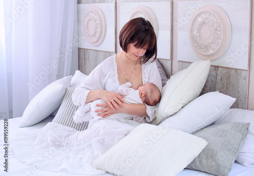 Obraz na płótnie Breastfeeding baby. Young mother holding her newborn child. Mom nursing baby. Woman and new born relax in a white bedroom. Mother breast feeding baby. w salonie