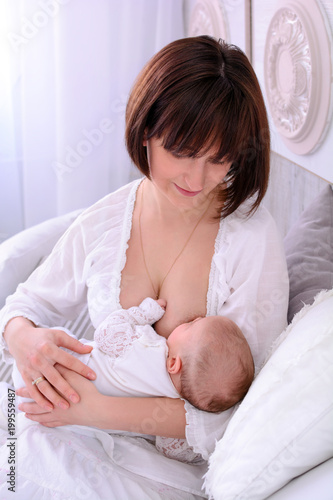 Obraz na płótnie Breastfeeding baby. Young mother holding her newborn child. Mom nursing baby. Woman and new born relax in a white bedroom. Mother breast feeding baby. w salonie