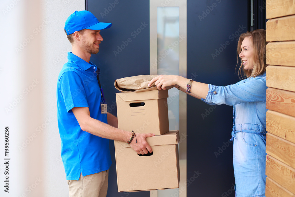 Smiling delivery man in blue uniform delivering parcel box to recipient - courier service concept. Smiling delivery man in blue uniform Smiling delivery man in blue uniform delivering parcel box to recipient - courier service concept. Smiling delivery man in blue uniform