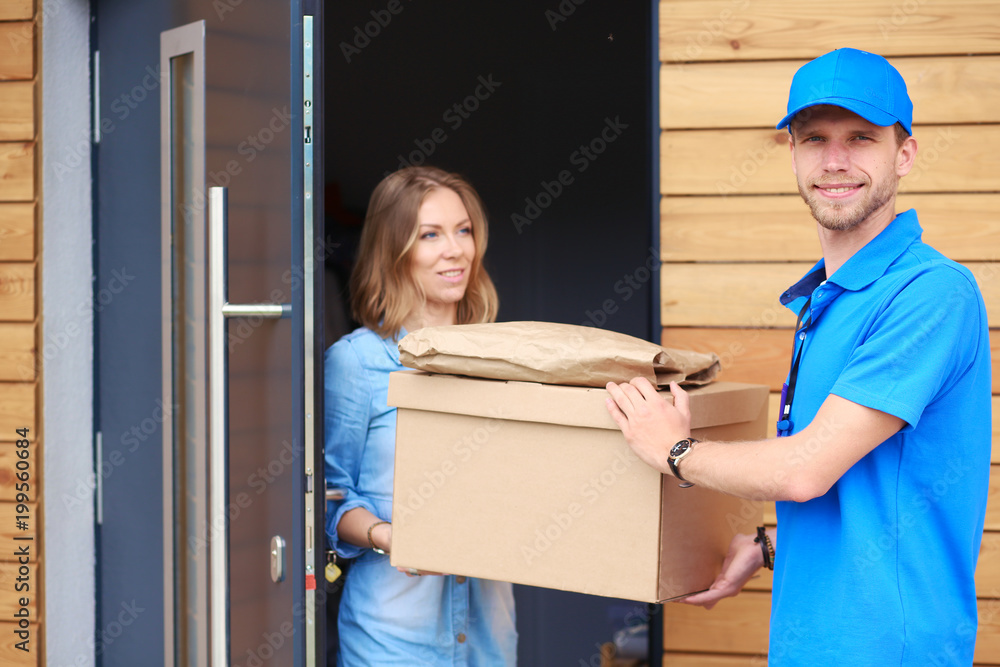 Smiling delivery man in blue uniform delivering parcel box to recipient - courier service concept. Smiling delivery man in blue uniform Smiling delivery man in blue uniform delivering parcel box to recipient - courier service concept. Smiling delivery man in blue uniform
