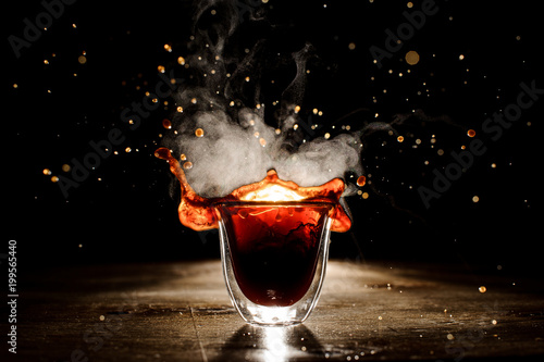 Splash of the coffee from the transparent glass on the dark background