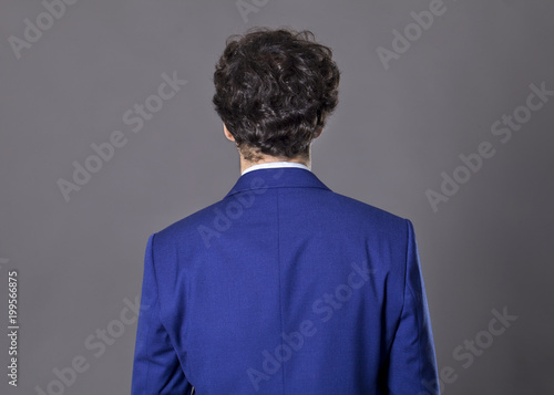 Young man with curly hair standing back to camera