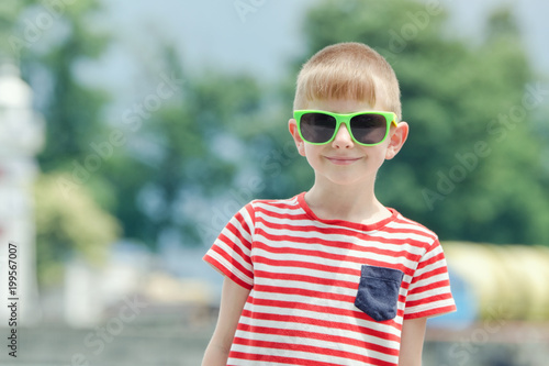 Boy in a striped T-shirt and glasses stands against the background of the sea. Portrait © somemeans