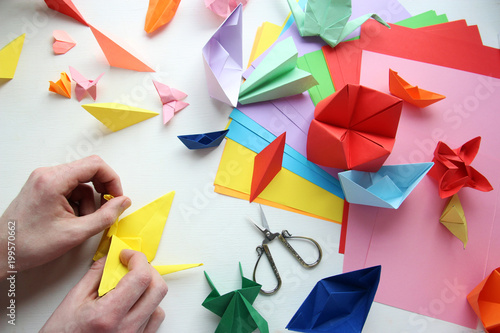 Man doing origami. Multicolored Origami and paper on  a white table.