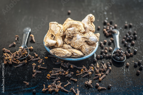 Close up of ayurvedic herb or folk medicine Dried Ginger or Zingiber officinale with black pepper corns and cloves on wooden surface with benefits like relieving nausea, loss of appetite etc. photo