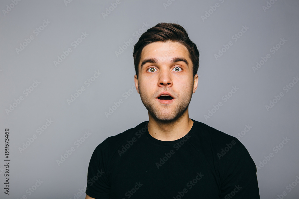 Obraz premium Surprised. Handsome young man standing against grey background.