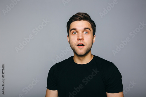 Surprised. Handsome young man standing against grey background.