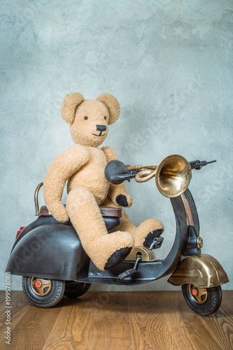 Foto op Aluminium Teddybeer zittend op oude retro speelgoed scooter met klassieke claxon vooraan betonnen getextureerde muur achtergrond. stijl gefilterde foto -