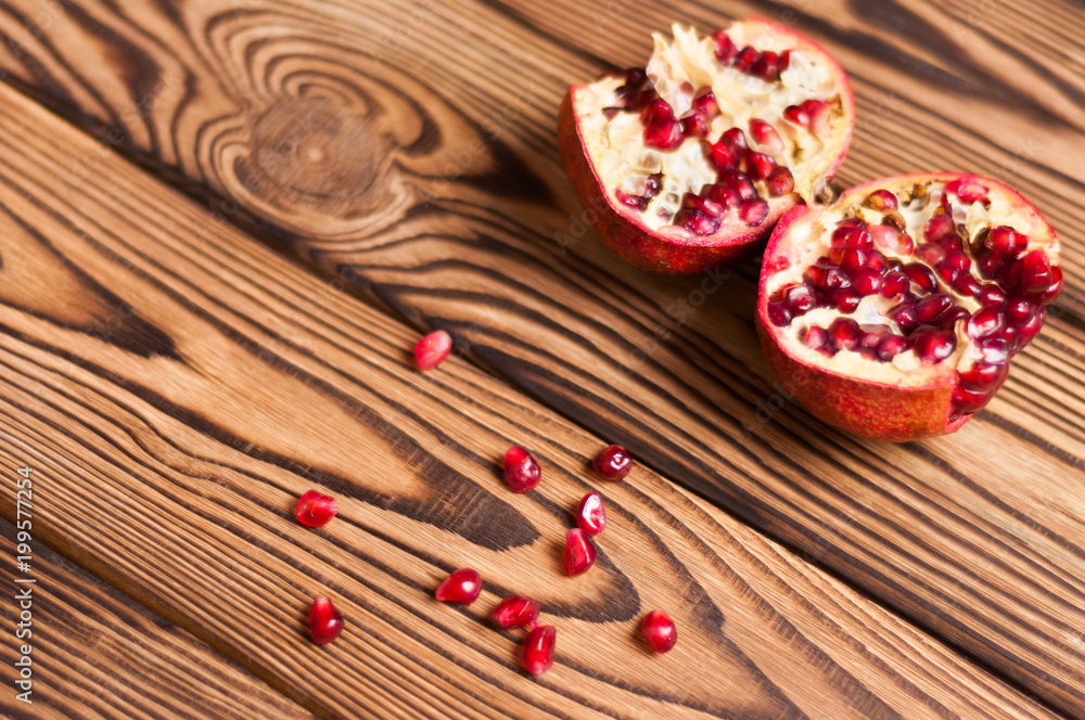 Scattered fresh ripe red seeds of pomegranate near two half pomegranate on old brown weathered wooden planks Scattered fresh ripe red seeds of pomegranate near two half pomegranate on old brown weathered wooden planks