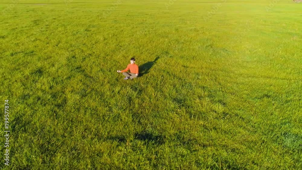 UHD 4K aerial view. Low altitude radial flight over sport yoga man at perfect green grass. Sunset in mountain. Green meadow and sun rays on horizon. Fast orbital movement. UHD 4K aerial view. Low altitude radial flight over sport yoga man at perfect green grass. Sunset in mountain. Green meadow and sun rays on horizon. Fast orbital movement.