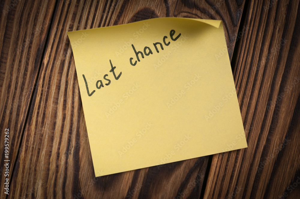Black handwritten inscription last chance on yellow square sticky sticker on old wooden brown table Black handwritten inscription last chance on yellow square sticky sticker on old wooden brown table