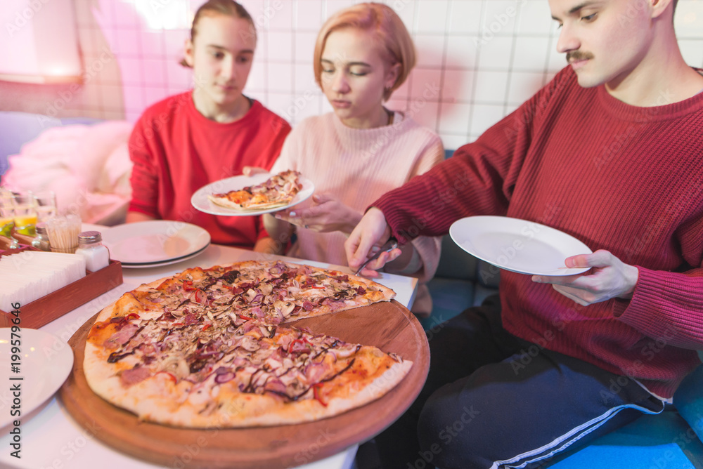 A group of friends sits in a pizzeria and eats a big pizza. Young people eat pizza at the restaurant on weekends. A group of friends sits in a pizzeria and eats a big pizza. Young people eat pizza at the restaurant on weekends.