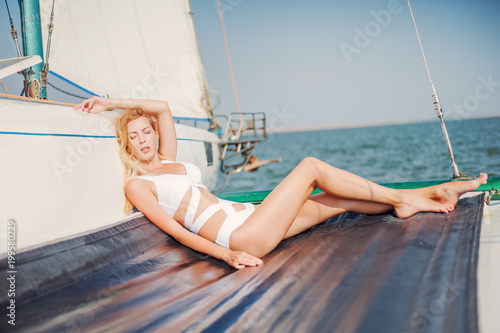woman in fashion white swimsuit sitting on yacht