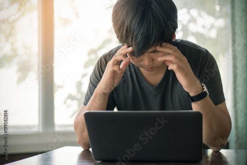 Asian young man resting his eye from work with laptop computer all day long and stressed. Male Have headache and migraine.