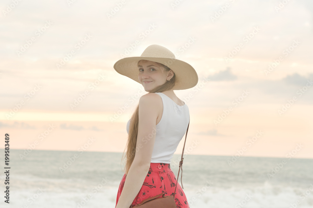 Girl in a hat on the beach and smiling sweetly. Sunset time