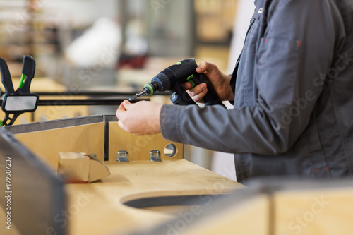 production, manufacture and industry concept - assembler working with electric screwdriver making furniture at workshop