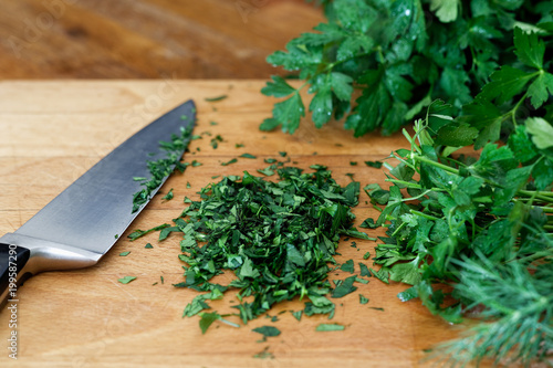 Freshly chopped up bunch of parsley on wood chopping board next to kitchen knife.