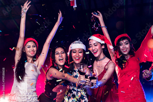 Group of happy young lady dancing together at nightclub with smoke and laser light. Friends celebrates new year together and disc jockey mixing music on background.