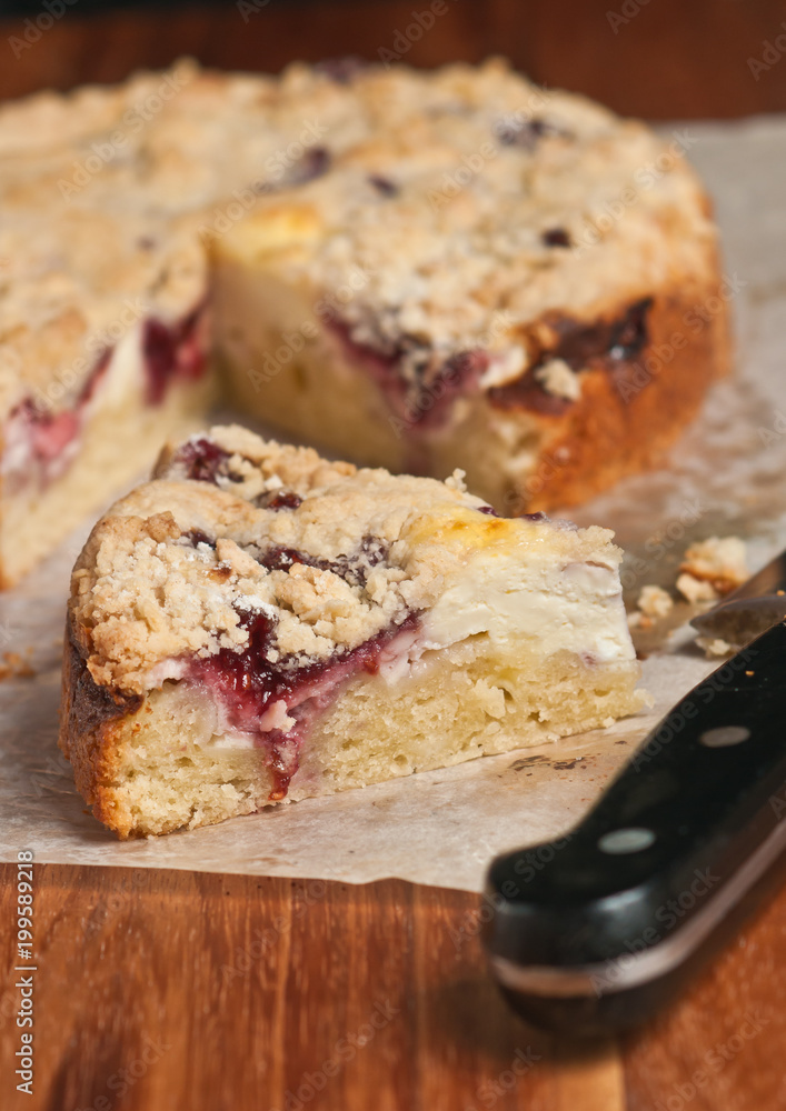 Fototapeta premium Top view, close up of a slice of freshly baked, homemade, raspberry cream coffee cake on a sheet of parchment paper with the handle of a chef's knife on a wood, cutting board 