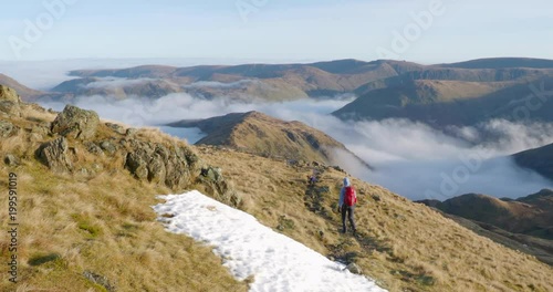 A hiker and their dog descending Hart Crag by Hartsop Above How with a cloud inversion below in the English Lake District, UK.