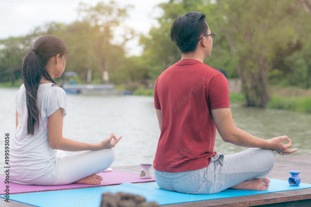 Young couple sitting on the mat beside the lake and doing meditation together. Young couple sitting on the mat beside the lake and doing meditation together.
