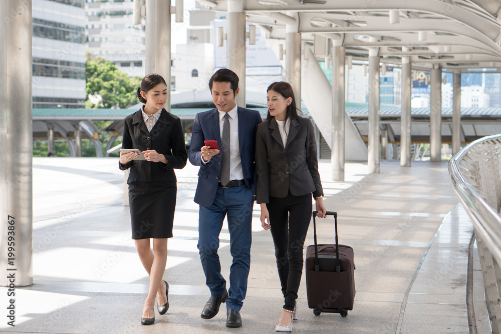 Group of business people checking flight from mobile phone during walk to check in at airport. Boss sending staff / employee to business trip conference. Group of business people checking flight from mobile phone during walk to check in at airport. Boss sending staff / employee to business trip conference.