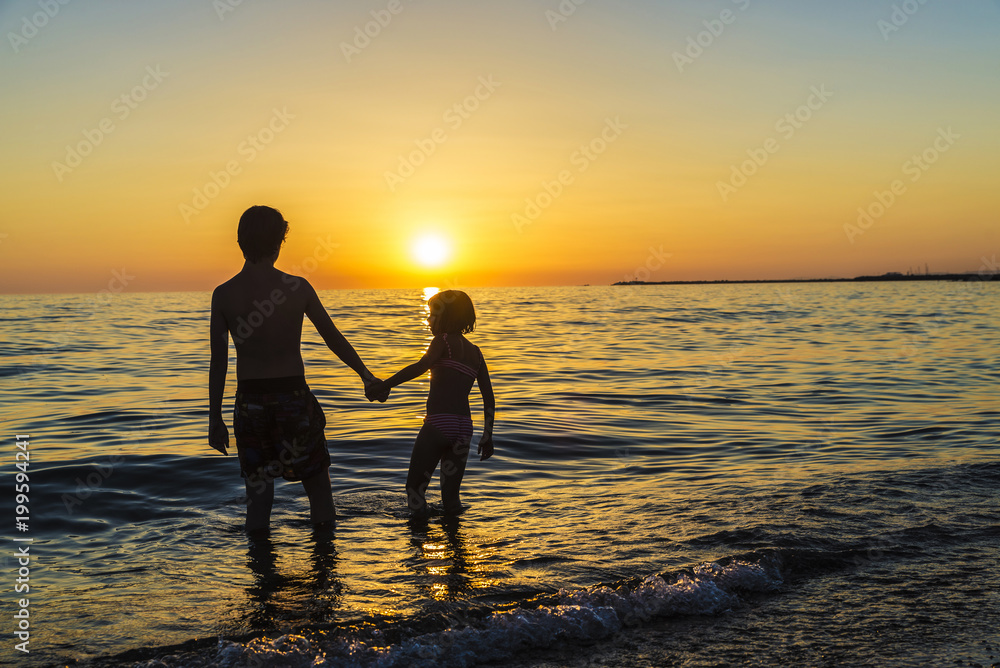 Little girl and teenager bathing on a beach at sunset