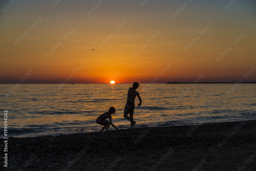 Little girl and teenager playing on a beach at sunset