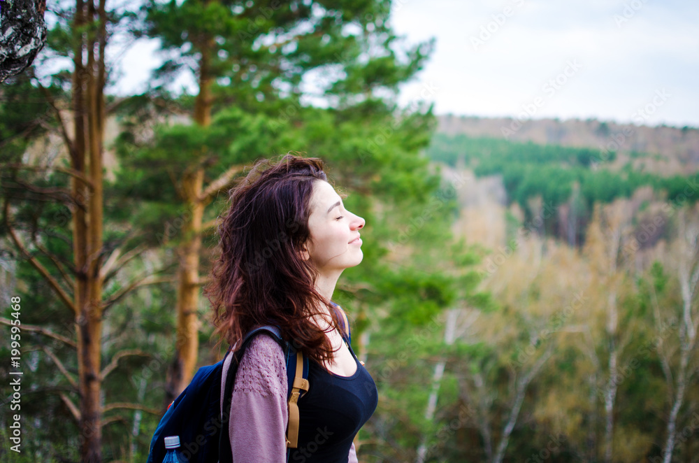 Young beautiful girl looks into the distance and enjoys the beauty of the forest, the wind blows her hair