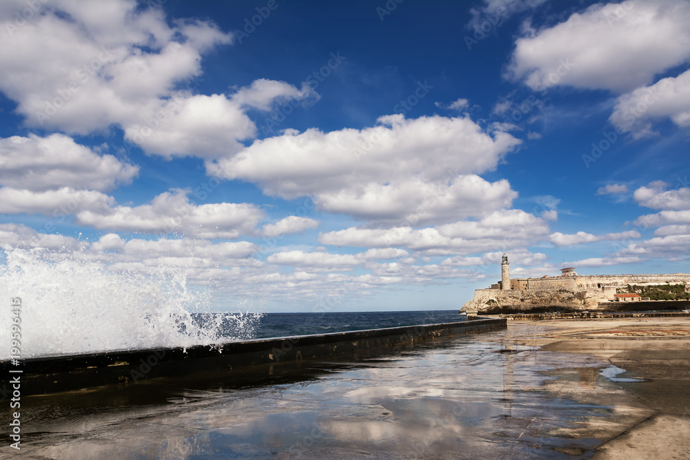 Promenade of the Malecon of Havana, Morro Castle and its lighthouse with crashing waves