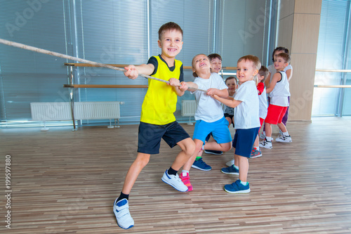 Children and recreation, group of happy multiethnic school kids playing tug-of-war with rope in gym