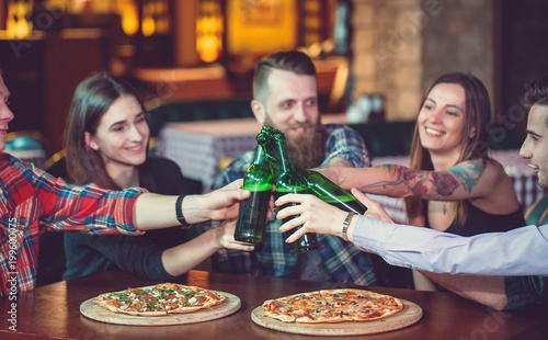 Wallpaper Mural Friends having a drinks in a bar, They are sitting at a wooden table with beers and pizza. Torontodigital.ca