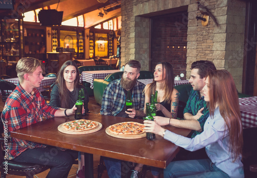Wallpaper Mural Friends having a drinks in a bar, They are sitting at a wooden table with beers and pizza. Torontodigital.ca