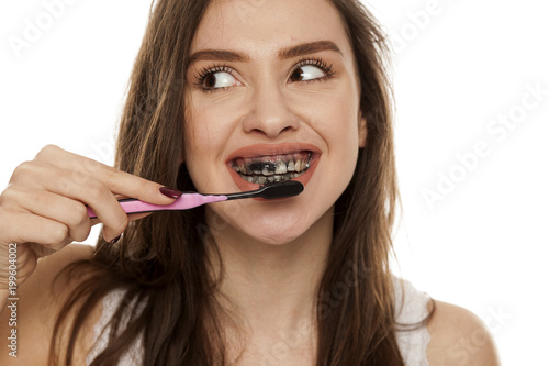 young woman brushing her teeth with a black tooth paste with active charcoal  and black tooth brush on white background  and showing thumbs up