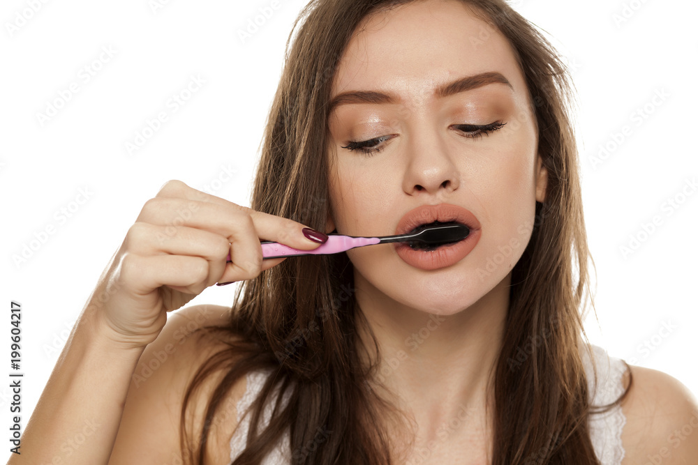 young woman brushing her teeth with a black tooth paste with active charcoal, and black tooth brush on white background young woman brushing her teeth with a black tooth paste with active charcoal, and black tooth brush on white background