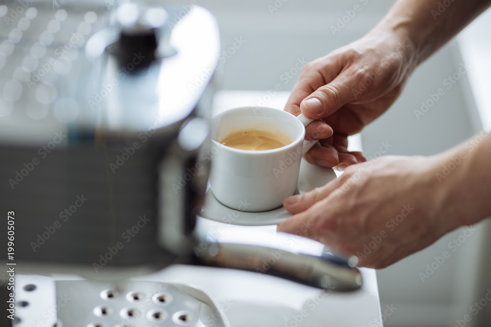 The man holds cup of espresso next to a coffee maker