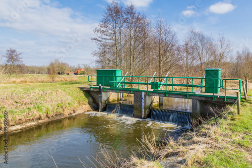 Narrow bridge over a small river in a nature reserve in the Netherlands. There is a weir under the bridge. It is at the end of the winter season.