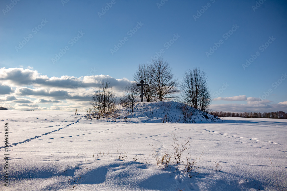 Barrow with an Orthodox cross in the middle of the snow-covered field