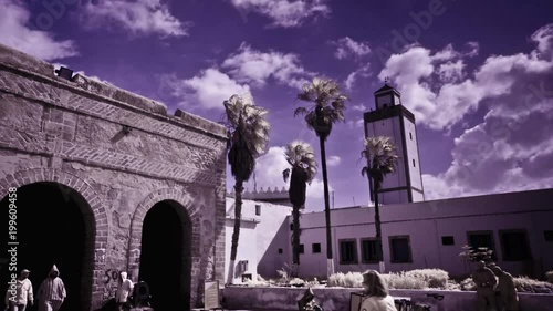 Minaret and old city arches marking the entrance to Essaouira Morocco in an infrared time lapse with blue sky and big puffy clouds