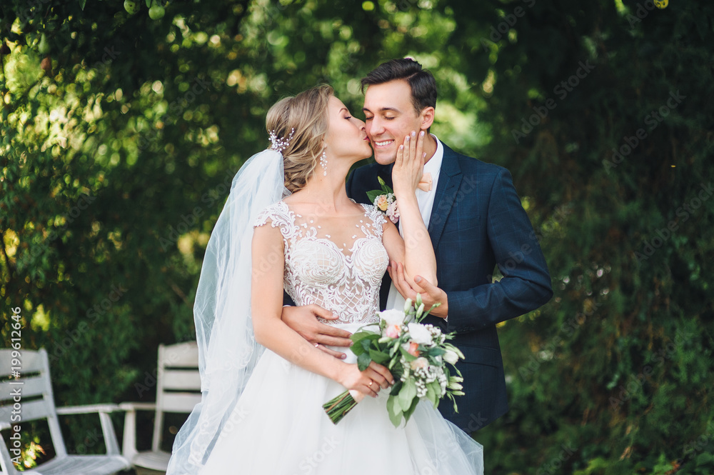 Cute newlyweds hugging and smiling in a green park. Portrait of the bride and groom in a lace dress. Cute newlyweds hugging and smiling in a green park. Portrait of the bride and groom in a lace dress.