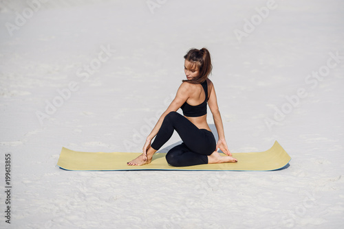 Fitness girl doing stretching on the beach. Female athlete doing a warm up on yoga mat. Sport yoga and healthy lifestyle concept.