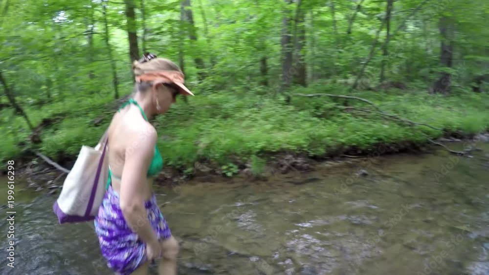 Bikini clad mature woman hiking through natural mountain stream or creek in forest, captured with steadicam Bikini clad mature woman hiking through natural mountain stream or creek in forest, captured with steadicam