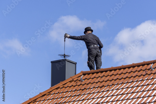 Chimney sweep cleaning a chimney standing on the house roof, lowering equipment down the flue