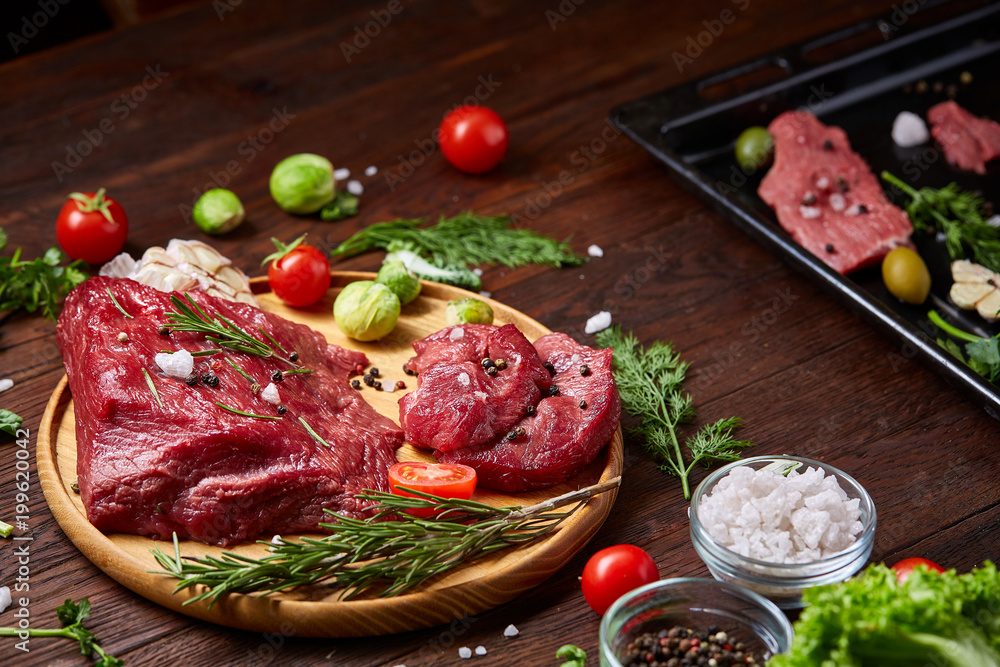Flat lay of raw beefsteak with vegetables, herbs and spicies on metal tray, close-up, selective focus