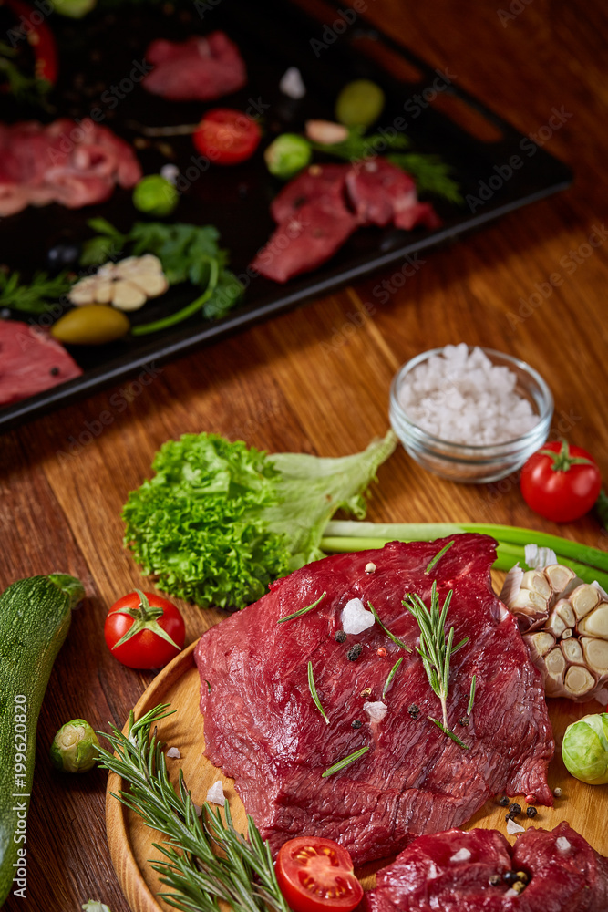 Still life of raw beef meat with vegetables on wooden plate over white background, top view, selective focus Still life of raw beef meat with vegetables on wooden plate over white background, top view, selective focus
