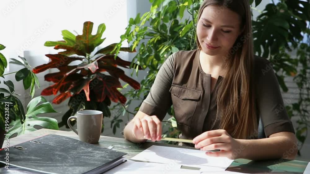 work at home. young beautiful freelancer woman is working at the table by the window in the house. modern ecological interior with living plants. work at home. young beautiful freelancer woman is working at the table by the window in the house. modern ecological interior with living plants.